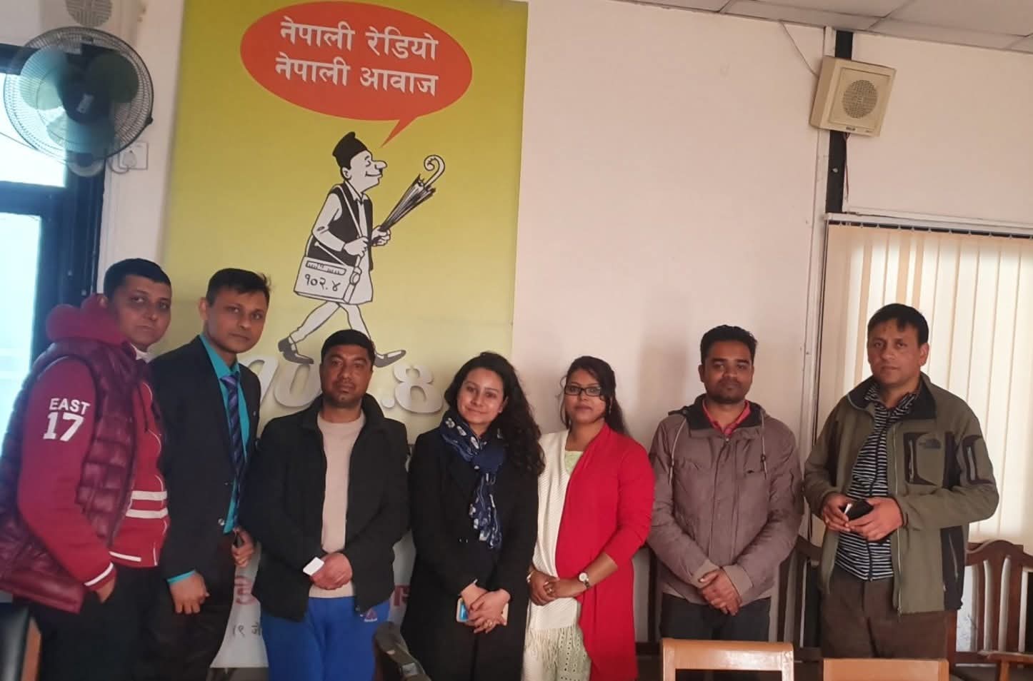 Team gathered under a Nepali radio station banner reading Nepali Radio, Nepali Voice