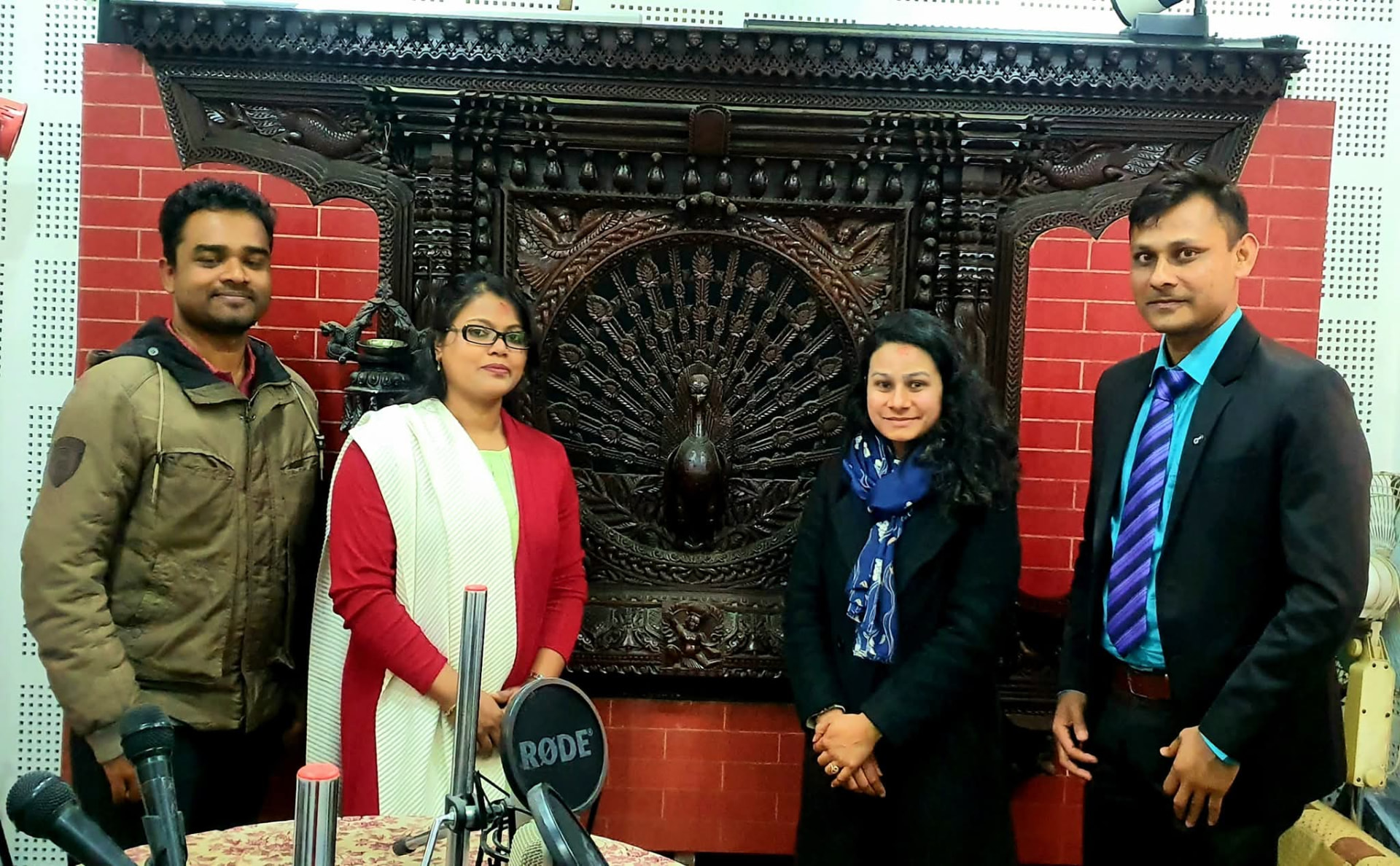 Exchange team at a Nepali community radio station in front of traditional carved woodwork